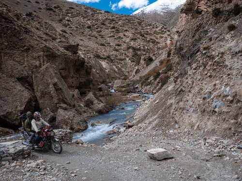 The track into upper Dolpo: motorcycle and passengers cross a river gorge below snow peaks. The road ends here; the rest is on foot.