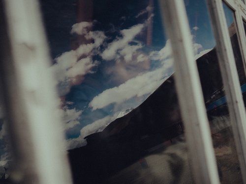 Sky and peaks reflected in a south-facing window pane. The aperture functions simultaneously as weather barrier and solar collector.