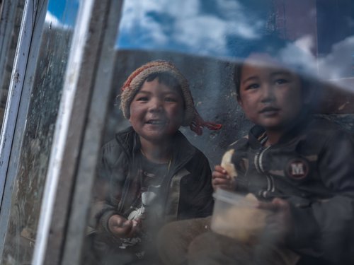Two children look in through a frost-hazed window. The temperature differential across a single-pane glass in October can exceed 20 °C.