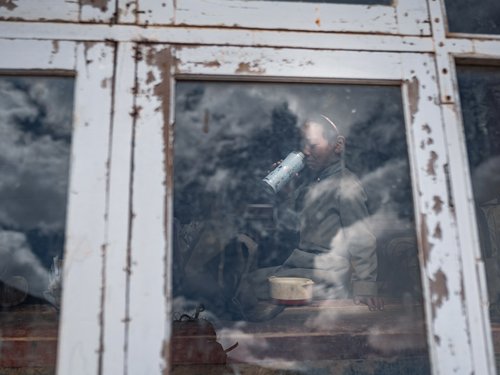 An elderly villager seen through the glass of a whitewashed building. The survey combined thermal measurement with structured household interviews.